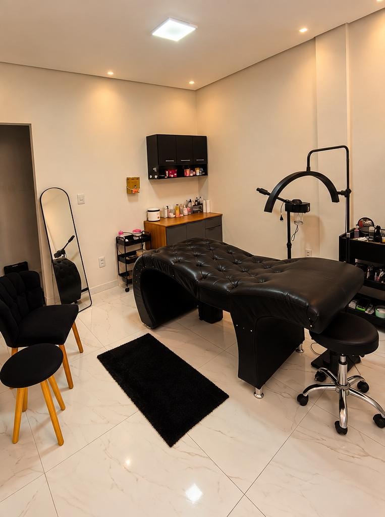 Sala de atendimento do Leide Sousa Studio com maca preta, luminária e organizadores